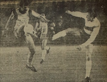 Imagen en blanco y negro de dos jugadores de fútbol en acción, uno saltando para golpear el balón y otro estirándose para interceptar