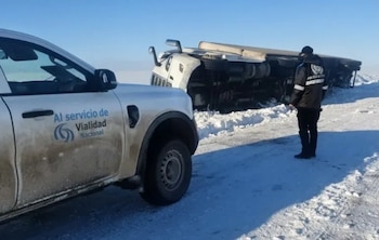 Un camión blanco volcado en una ruta con nieve, una camioneta gris con el logo de Vialidad Nacional y un hombre uniformado de espaldas