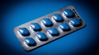 Diez pastillas azules de forma ovalada y el número 100 grabado en cada una, dentro de un blíster plateado sobre fondo azul.