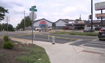 Vista diurna de una intersección de calles en Austin con cinta policial amarilla que bloquea el paso; un coche de policía es visible a la derecha, y señales de calle muestran Burton y E Oltorf