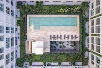 Vista aérea cenital de un complejo residencial blanco con una piscina rectangular azul rodeada de baldosas claras, tumbonas y densa vegetación verde