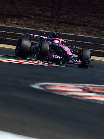 Un monoplaza de Fórmula 1 color rosa y azul circula en una pista de carreras con curvas señalizadas por bordillos rojos y blancos
