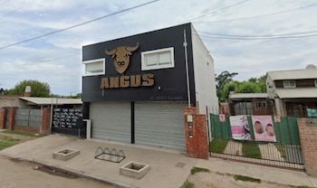 Fachada de la carnicería Angus, un edificio negro con logo de toro y letras doradas, con dos persianas metálicas cerradas y ventanas blancas arriba