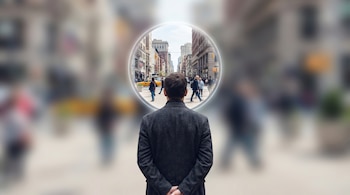 Hombre de espaldas en primer plano, con un círculo nítido frente a su cabeza que muestra una calle urbana con edificios, personas y un taxi amarillo.