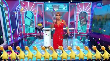 Magaly Medina viste un vestido rojo en un estudio iluminado con confeti cayendo y una hilera de patos amarillos animados