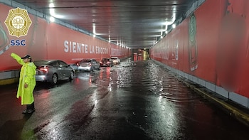 Agente de tránsito con impermeable amarillo dirige el tráfico en túnel vehicular inundado con varios coches detenidos y publicidad de Subway en las paredes