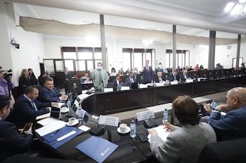 Autoridades y asistentes sentados alrededor de una mesa curva con micrófonos frente al emblema del Congreso de la República de Guatemala