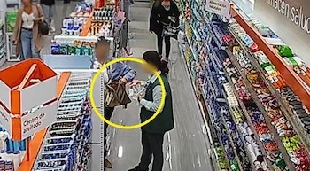 Imagen de seguridad de un supermercado, mostrando a un cliente interactuando con un empleado con chaleco verde junto a estanterías de productos