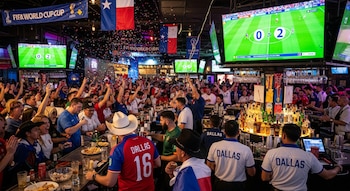 Multitud de personas animan en un bar abarrotado de Dallas, con pantallas mostrando un partido de fútbol, confeti cayendo y camareros sirviendo bebidas.