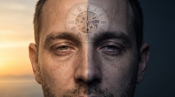 Primer plano de un rostro de hombre, dividido verticalmente entre luz de amanecer y oscuridad, con un reloj analógico semitransparente en la frente.