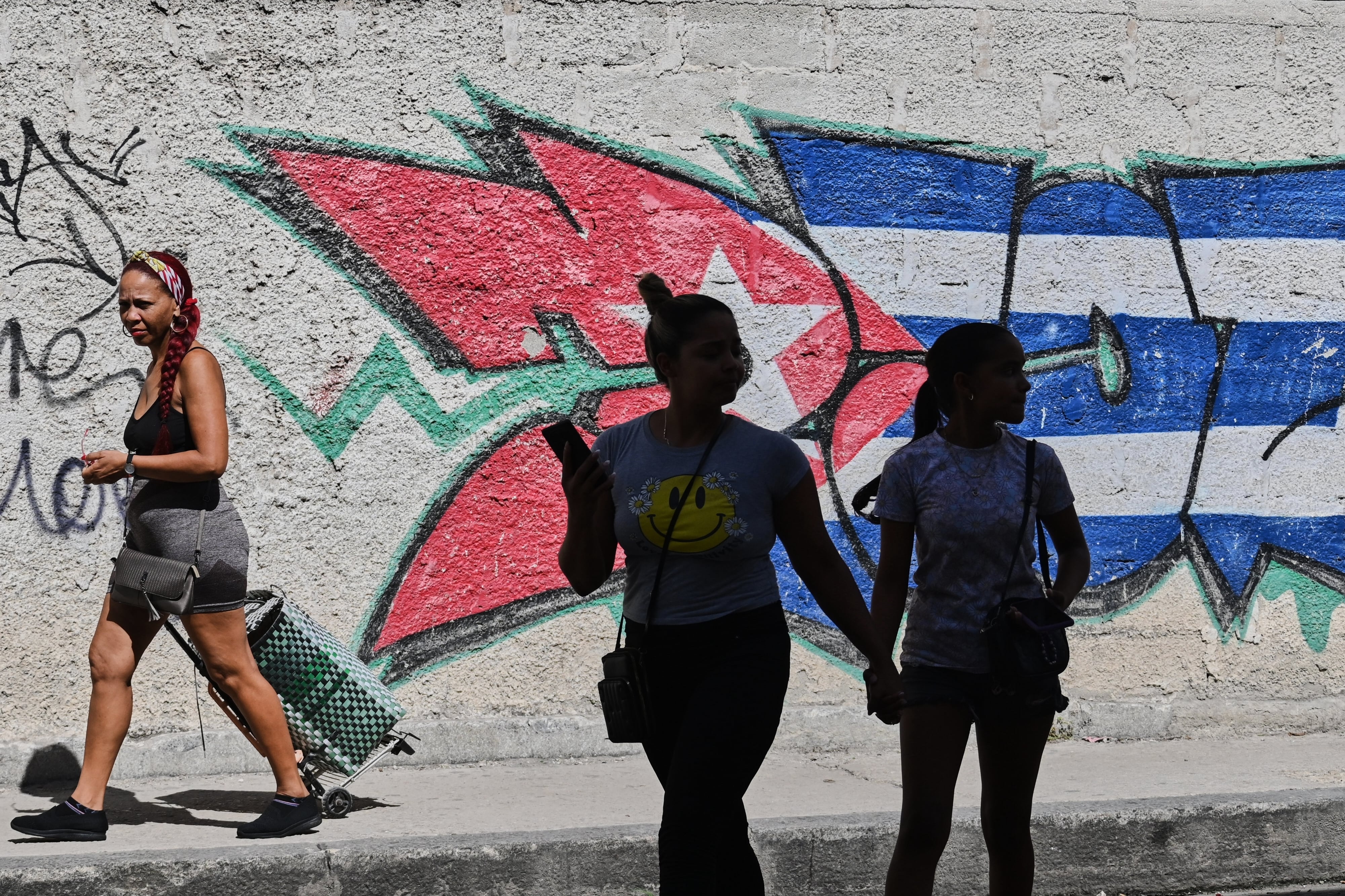 Varias personas pasan junto a grafitis con los colores de la bandera cubana en La Habana, Cuba, el miércoles 17 de junio de 2026 (Foto AP/Jorge Luis Baños)
