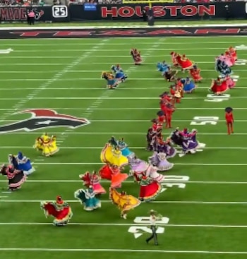 Bailarines con trajes folklóricos de colores brillantes realizan una coreografía en un campo verde de fútbol americano con números marcados