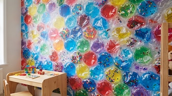Plástico de burbujas de distintos colores instalado en una pared junto a un escritorio pequeño y juguetes de madera.