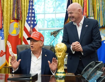 Donald Trump, sentado, gesticula con una gorra roja mientras Gianni Infantino sonríe de pie junto al trofeo de la Copa Mundial de la FIFA en la Oficina Oval
