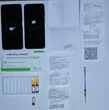 Varias jeringas plásticas, agujas hipodérmicas en sus empaques, una caja de clenbuterol y el borde de una computadora portátil sobre un mantel