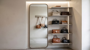 Espejo de cuerpo entero y estantes iluminados exhiben bolsos de cuero en tonos marrones, negros y beige, algunos colgados y otros dispuestos.