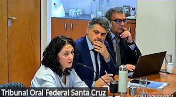 Tres personas sentadas en una mesa con micrófonos y una computadora portátil. Una mujer habla, dos hombres la escuchan. Fondo de pared y muebles