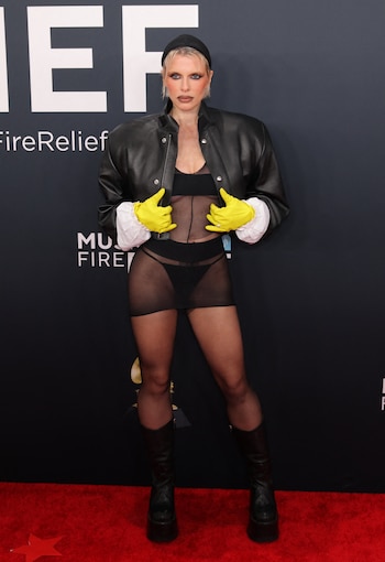 La actriz Julia Fox hizo una declaración audaz con un look compuesto por una chaqueta de cuero negra de hombros estructurados, un corsé transparente y shorts negros estilo lencería. Complementó su atuendo con guantes amarillos brillantes, medias transparentes y botas de plataforma negras