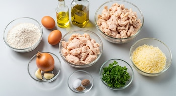 Vista aérea de ingredientes para ravioles: harina, huevos, aceite, pollo cocido y picado, cebolla, ajo, perejil, queso rallado, sal, pimienta y nuez moscada en cuencos.