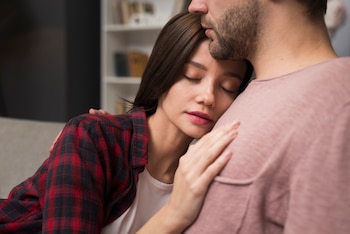 Una mujer con los ojos cerrados se apoya sobre el pecho de un hombre, al que solo se le ve a partir de la boca