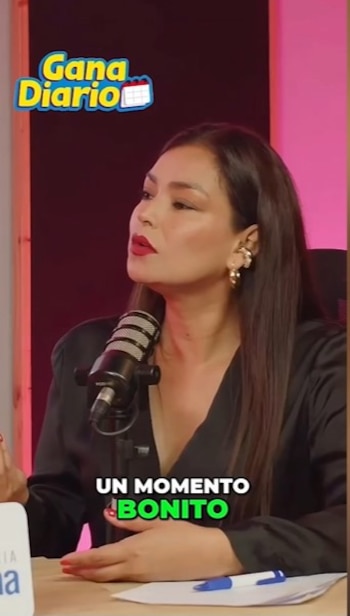 Claudia Portocarrero sentada frente a un micrófono en un estudio, vistiendo una blusa oscura, con cabello largo y labios rojos