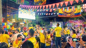 Multitud con camisetas amarillas, pantalla gigante en la calle. Banderas de países, banderines, teléfonos móviles grabando, globos de colores.
