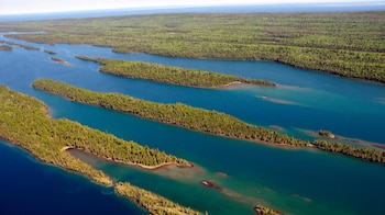 Vista aérea de varias islas largas y estrechas cubiertas de árboles verdes densos, separadas por canales de agua azul y verde turquesa, con un horizonte distante