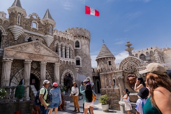 Edificio de piedra estilo castillo con torres, arcos, un letrero que dice "Camelot", una bandera de Perú en lo alto y visitantes caminando por el patio