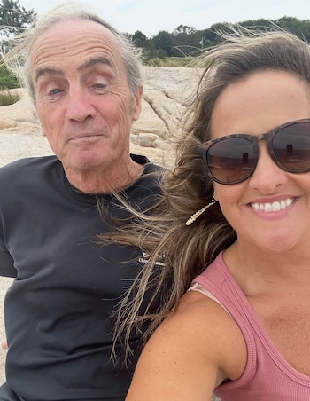 Selfie de un hombre mayor con cabello gris y una mujer sonriente con gafas de sol. Ambos tienen el pelo revuelto por el viento, al aire libre sobre rocas