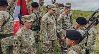 Soldados con uniformes de camuflaje de Perú y EE UU, algunos con boinas negras y fusiles, se congregan al aire libre bajo un cielo nublado