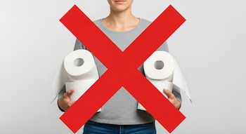 Vista frontal del torso de una persona sosteniendo dos paquetes de rollos de papel higiénico, con una gran 'X' roja brillante cubriendo la imagen.