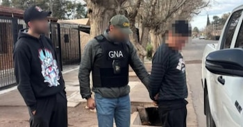 Tres hombres en una calle, uno de ellos con uniforme de Gendarmería Nacional Argentina, sujeta por el brazo a otro hombre junto a una camioneta blanca