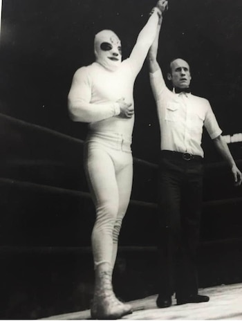 Fotografía en blanco y negro de un luchador enmascarado de blanco junto a un árbitro que le levanta el brazo sobre un cuadrilátero
