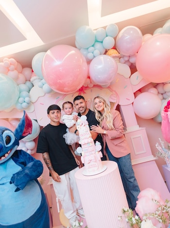 Cuatro personas posan junto a un pastel pastelero en una fiesta decorada con globos de colores y un personaje infantil azul