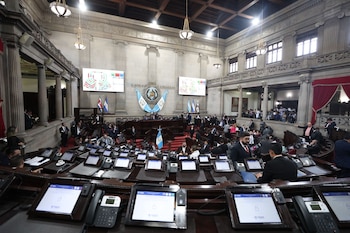 Vista amplia del hemiciclo del Congreso de la República de Guatemala, con numerosos diputados en sus curules, pantallas digitales y la bandera nacional al fondo