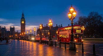 Torre del reloj Big Ben, Palacio de Westminster, un autobús rojo de dos pisos, farolas, puente, vehículos, personas y reflejos de luz en el pavimento.