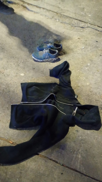 Un chándal negro y un par de zapatillas deportivas azules con cordones blancos yacen sobre una superficie de hormigón gris