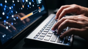 Manos sobre un teclado iluminado junto a una pantalla oscura con gráficos de nodos azules y una barra de progreso naranja.
