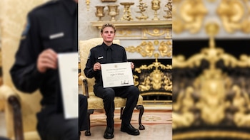 Hombre joven de uniforme oscuro sentado en una silla dorada, sostiene un certificado. De fondo se observa una chimenea ornamentada y objetos dorados