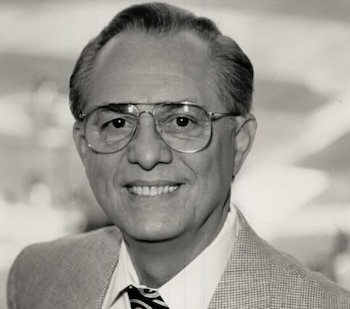 Retrato en blanco y negro de René Cárdenas, un hombre de mediana edad con gafas y sonrisa, vistiendo traje y corbata, mirando al frente