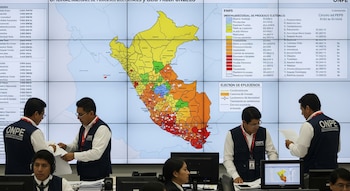 Trabajadores de la ONPE revisan documentos frente a una gran pantalla que muestra un mapa del Perú dividido por regiones con datos de resultados electorales.