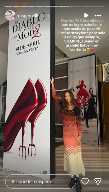 Natalie Vértiz posa sonriente junto a un póster de ‘El diablo viste a la moda 2’ con tacones rojos en forma de tridente; otro póster de la película está detrás