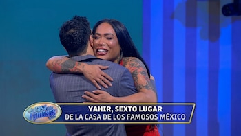 Una mujer con tatuajes en los brazos abraza por el cuello a un hombre vestido con un saco gris a rayas