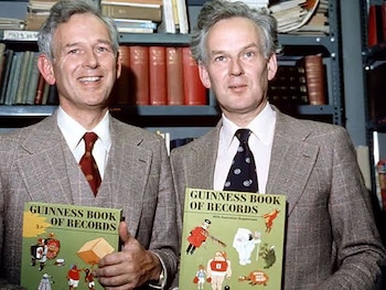 Dos hombres gemelos vestidos con traje sostienen ejemplares del libro Guinness Book of Records frente a estanterías con libros