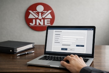 Una mano interactúa con el teclado de una computadora portátil abierta que muestra un formulario digital, junto a un logo del JNE y un archivador en un escritorio.