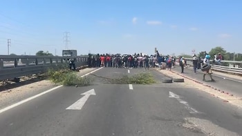 Vista general de una carretera o puente bloqueado por un grupo de personas. Se ven ramas y neumáticos en el asfalto. Al fondo, un autobús y torres eléctricas