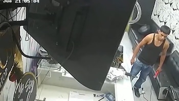 Vista de cámara de seguridad de un hombre con camiseta sin mangas y jeans azules sosteniendo un objeto rojo, de pie en un establecimiento
