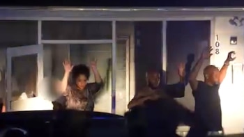 Cuatro personas con los brazos levantados frente a un edificio con el número 108 iluminado. Dos de ellas tienen las palmas abiertas