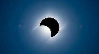 Cielo azul intenso con el Sol parcialmente cubierto por la Luna, mostrando el brillo del Sol alrededor del borde oscuro de la Luna.
