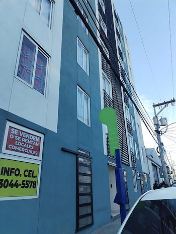 Fachada de edificio azul y blanco con letreros de venta/alquiler. Un poste eléctrico con cables y parte de un coche blanco se ven en primer plano